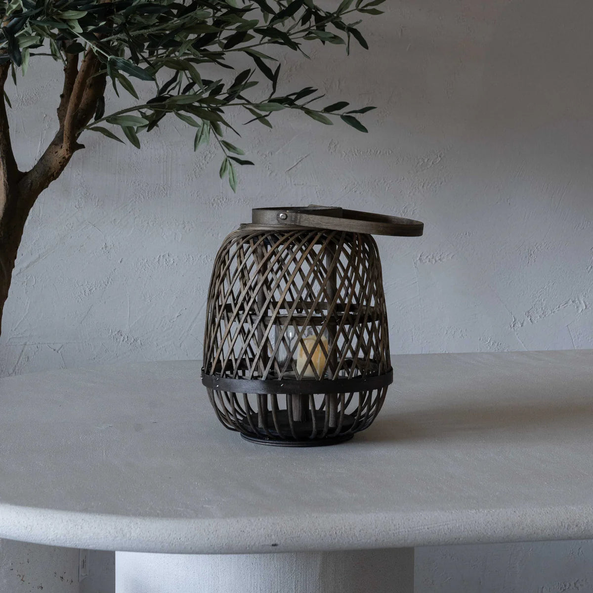 Woven lantern on a white surface with a plant in the background